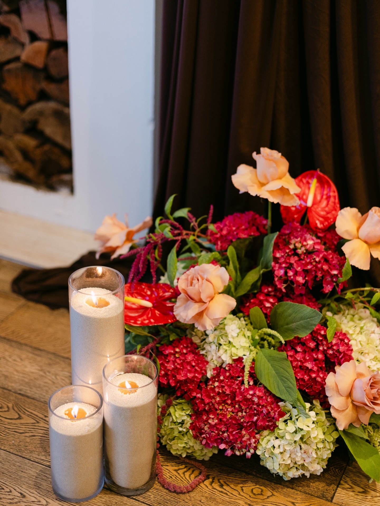 Arrangement of red hydrangea, peach roses and anthurium beside lit candles