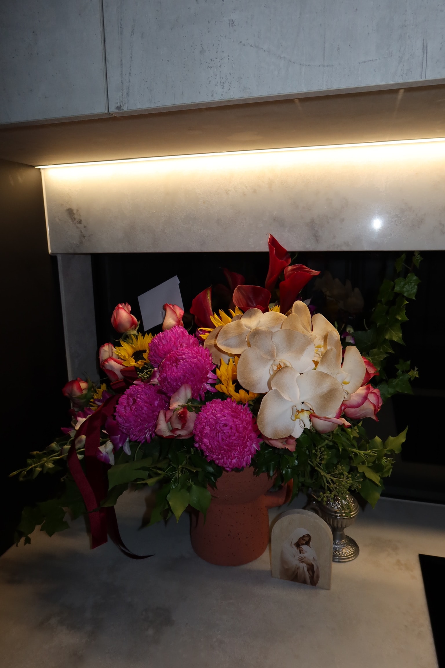 Memorial arrangement with red calla lilies, chrysanthemums and orchids beside a prayer card