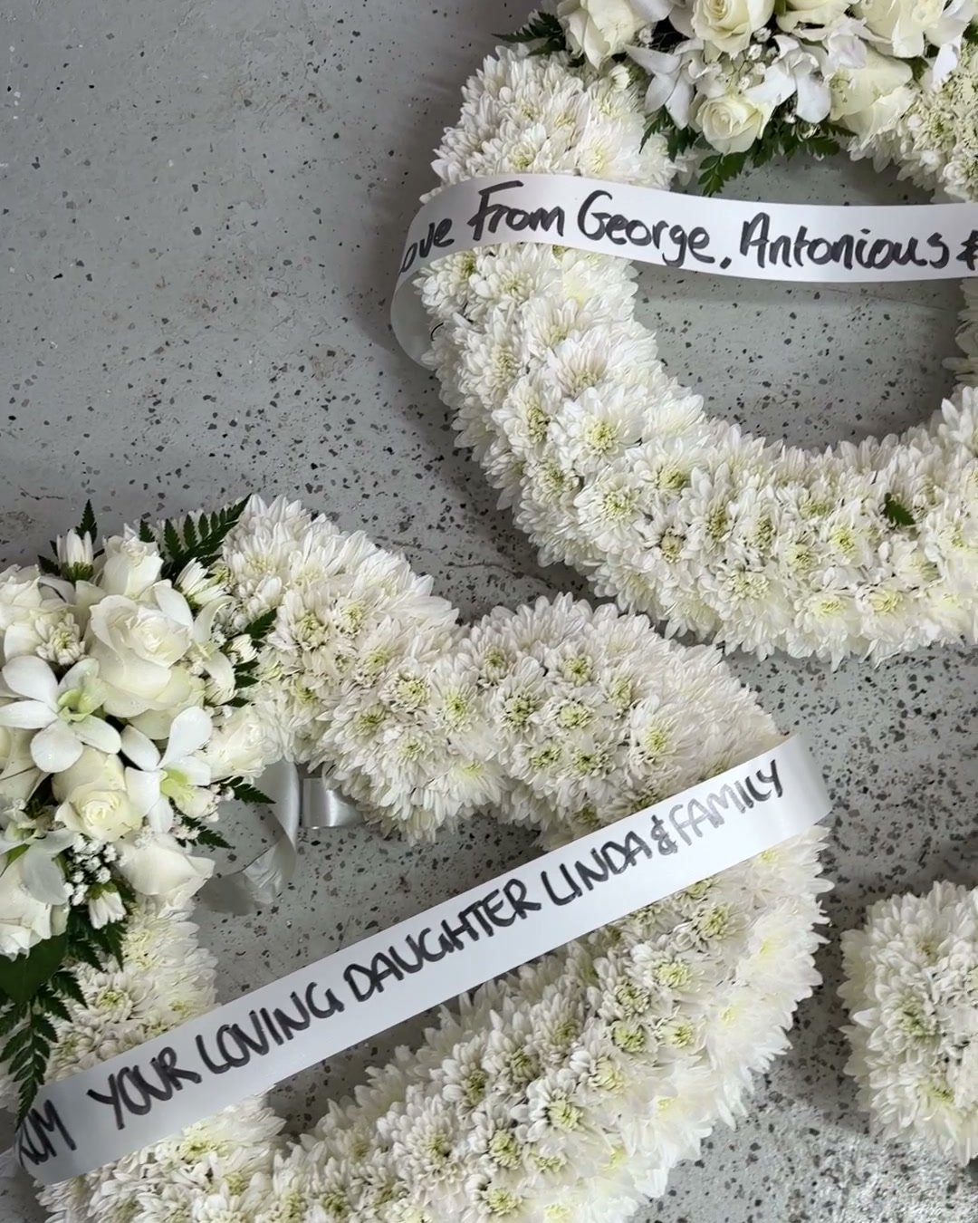 White chrysanthemum wreath, heart and cross tributes with message ribbons