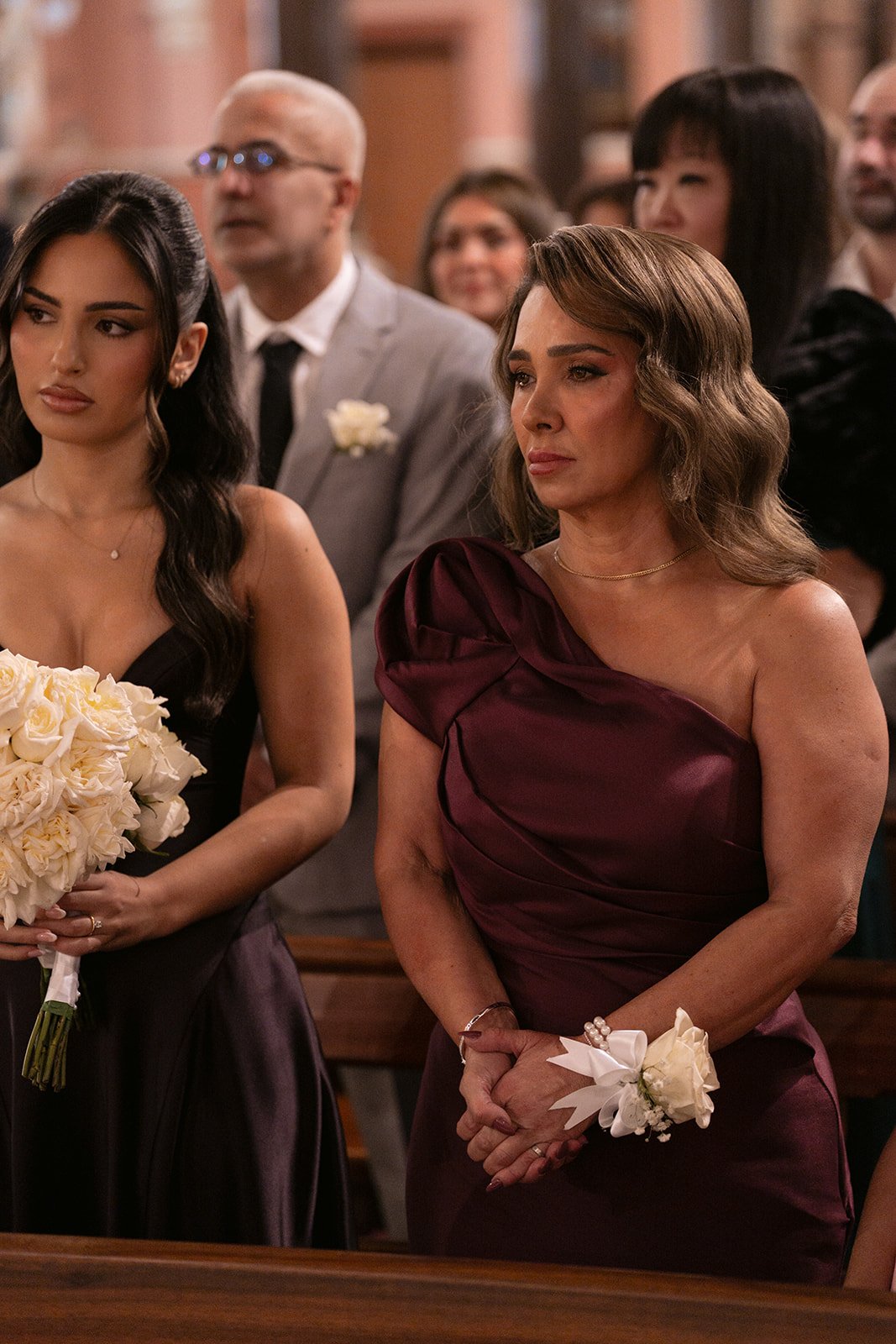 Bridesmaid holding an ivory rose bouquet beside a guest wearing a rose wrist corsage